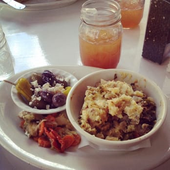 A sampler of marinated olives, feta and broccoli sides with a jar of juice